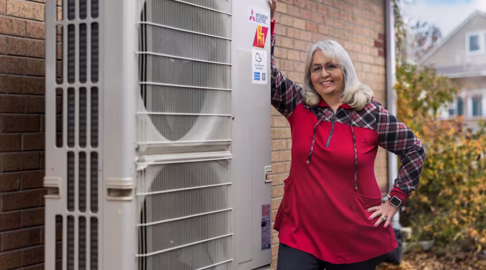 A woman in a red outfit with her arm on a tall heat pump smiling