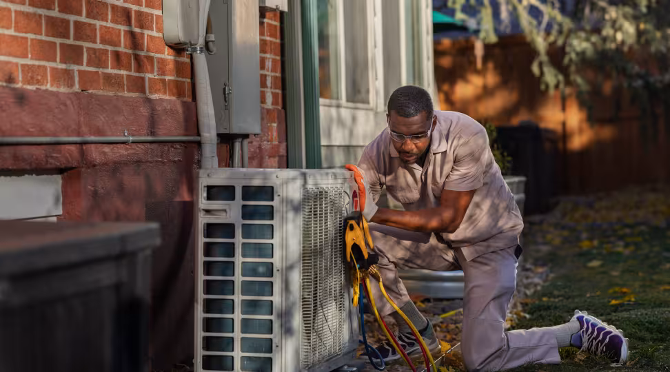 A HVAC worker using various tools to set up a heat pump on a brick home