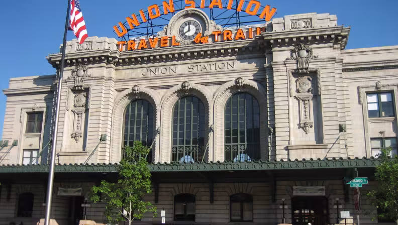 A grey building with large arching windows with orange "Union Station. Travel by Train" sign.