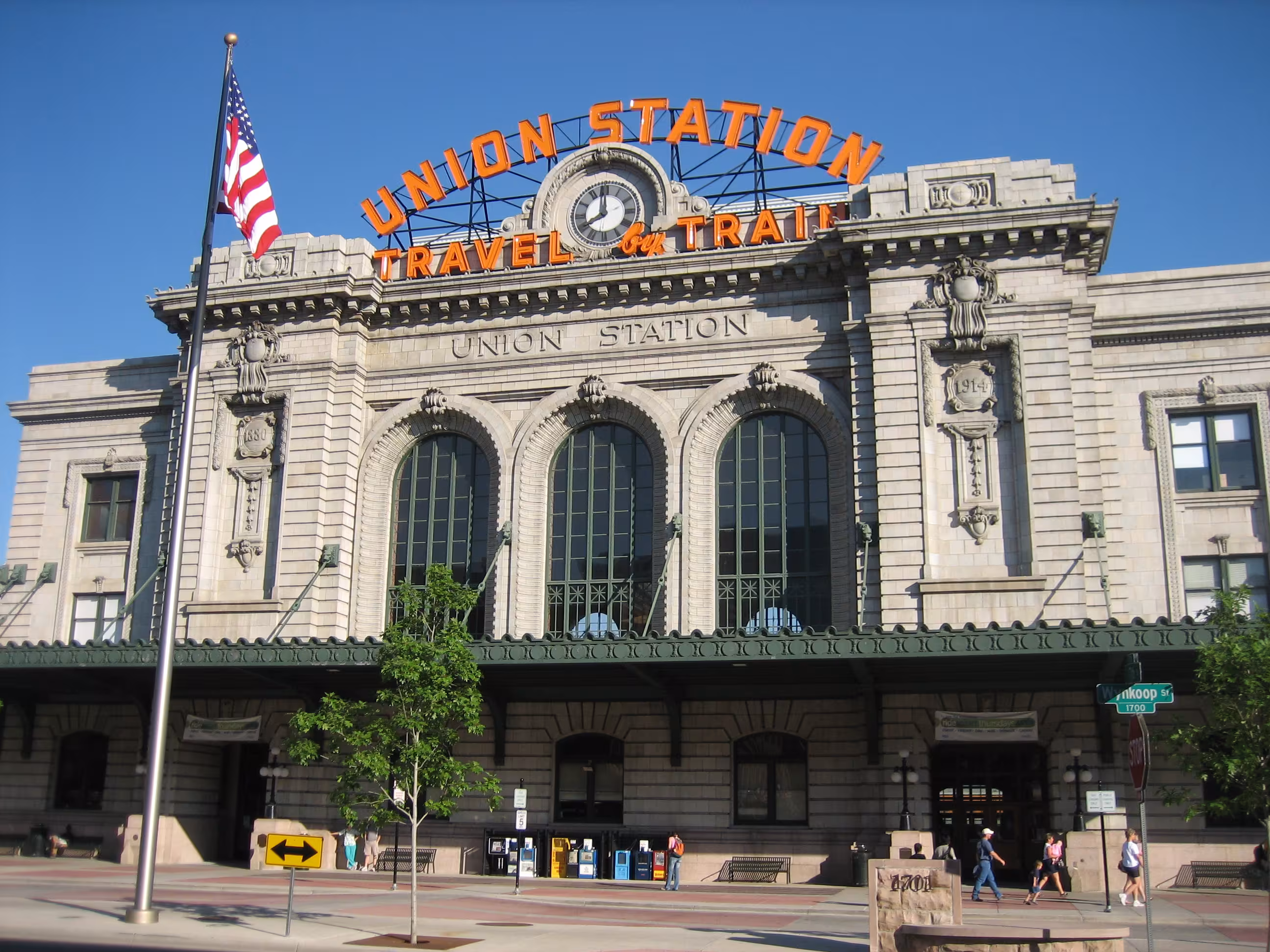A grey building with large arching windows with orange "Union Station. Travel by Train" sign.